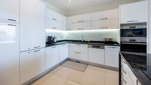 Una cocina moderna con armarios blancos, encimera negra y electrodomésticos de acero inoxidable.