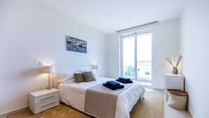 A modern bedroom with a large bed, bedside lamps, a view of the outdoors, and a small side table.