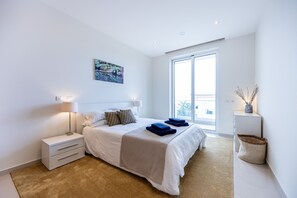 A modern bedroom with a large bed, bedside lamps, a view of the outdoors, and a small side table.