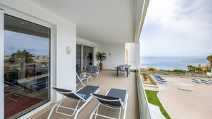 A balcony with outdoor seating, a dining table, and a view of the sea.