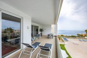 A balcony with outdoor seating, a dining table, and a view of the sea.