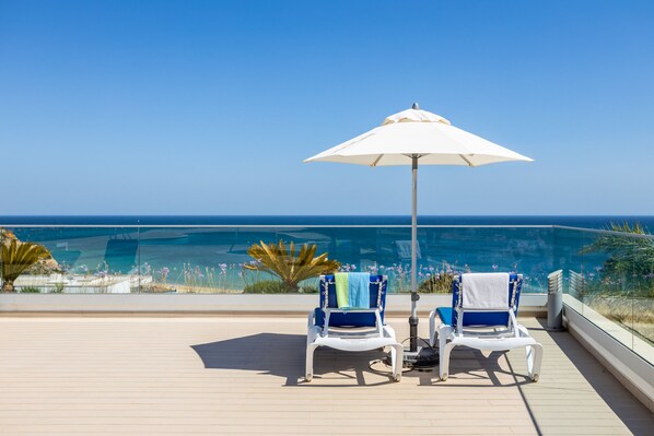 Two lounge chairs with towels, a white umbrella, and a view of the ocean. - CoolHouses Algarve Lagos | Amor à Vida T3 (Lagos)