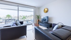 A modern living room with a large TV, comfortable seating, and a balcony with a view.