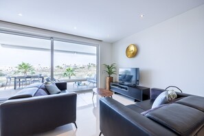 A modern living room with a large TV, comfortable seating, and a balcony with a view.