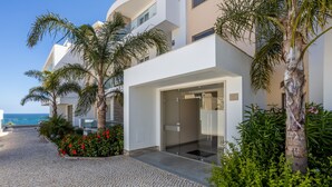 A modern building with a glass entrance, surrounded by palm trees and a cobblestone path.