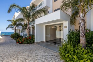 A modern building with a glass entrance, surrounded by palm trees and a cobblestone path.