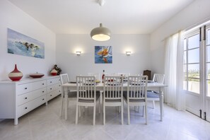 A dining area with a white table set for four, surrounded by white chairs. There are two wall-mounted light fixtures and a ceiling light. - CoolHouses Algarve Lagos | Casa Fernanda (Lagos)