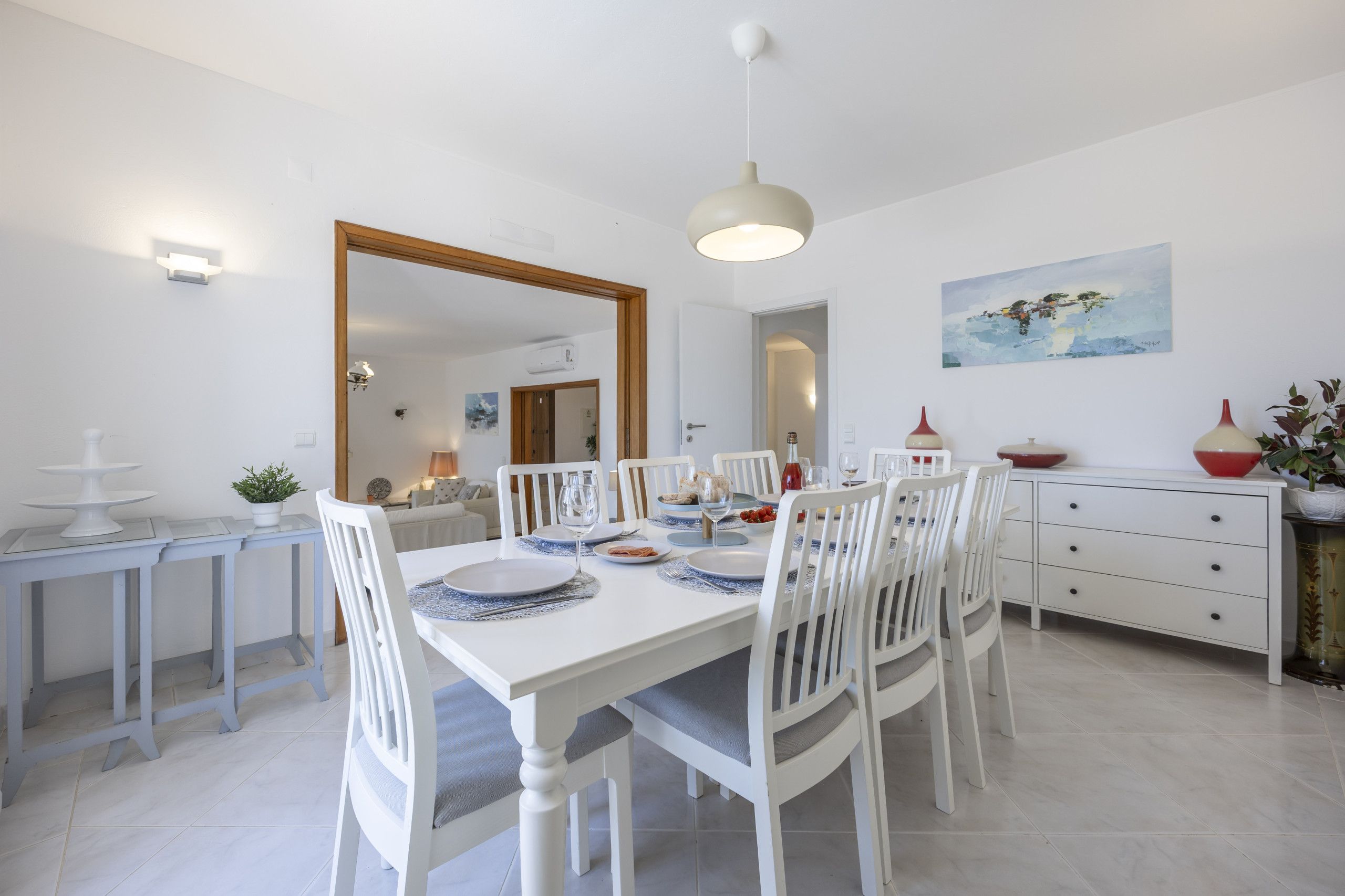 A dining area with a white table set for four, white chairs, and a large mirror on the wall.
