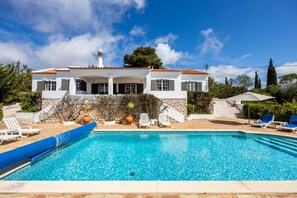 A white villa with a swimming pool, surrounded by greenery and a clear blue sky.