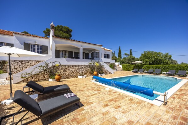 A poolside area with lounge chairs, a swimming pool, and a stone wall.