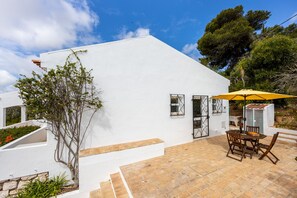 Edifici blanc amb zona de pati, taula i cadires, i un para-sol groc.