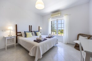 Habitació d'hotel amb un llit, taules de nit, una làmpada, una finestra amb cortines i una cadira de vimet.
