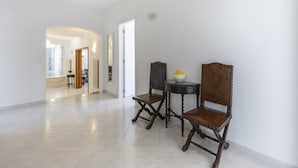 Un'ampia sala con un moderno lampadario, un'area pranzo con due sedie di legno e un tavolino, e uno specchio appeso al muro.