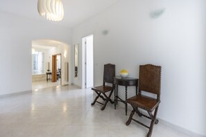 A spacious hallway with a modern light fixture, a dining area with two wooden chairs and a small table, and a mirror on the wall. - CoolHouses Algarve Lagos | Casa Fernanda (Lagos)