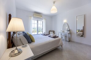 Ein Schlafzimmer mit Bett, Nachttisch, Lampe, Kommode, Spiegel und einem Fenster mit Vorhängen.
