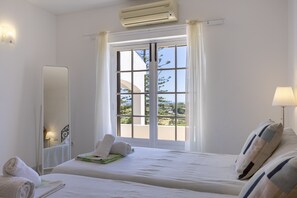 A hotel room with a bed, a window with curtains, a bedside lamp, and a wall-mounted air conditioner.