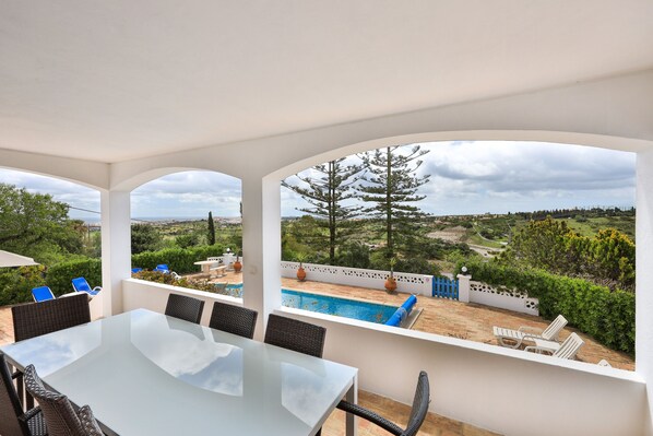 Zona exterior coberta amb piscina, taula de dinar i cadires, amb vista a un paisatge idíl·lic.
