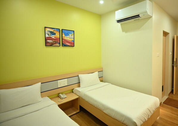 A hotel room with two single beds, a bedside table with a phone, an air conditioning unit, and two paintings on the wall. - Hotel City Centre Latur (Latur)