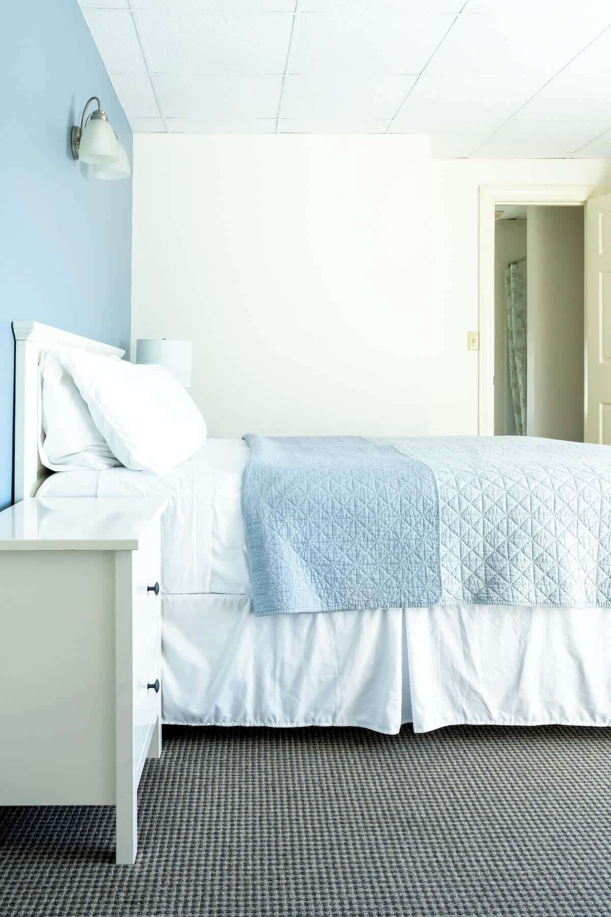 A neatly arranged hotel room with a bed, a bedside table, and a wall-mounted light fixture.