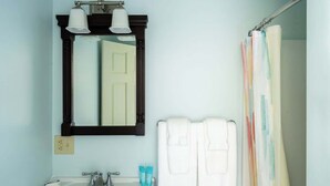 A bathroom with a white sink, two white towels, a mirror with a black frame, and a shower curtain with a colorful pattern. - #2 | Comfy Room w/ Queen-bed (Middletown)