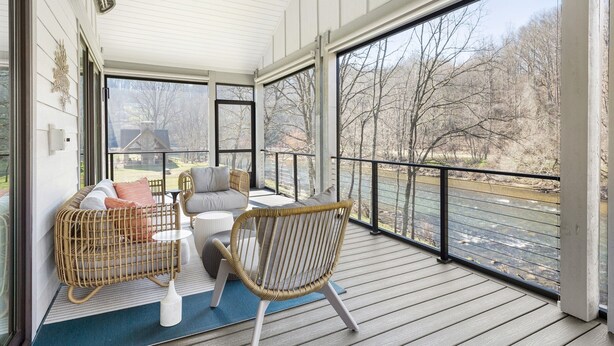 A covered porch with wicker furniture, a view of a river, and a clear sky. - Luxury Waterfront Getaway (Cullowhee)