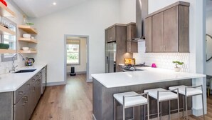 A modern kitchen with a central island, bar stools, and wooden cabinets. - Luxury Waterfront Getaway (Cullowhee)