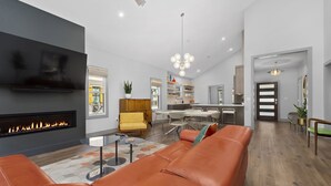 A modern living room with a fireplace, a sofa, a yellow armchair, and a dining area with a kitchen in the background. - Luxury Waterfront Getaway (Cullowhee)