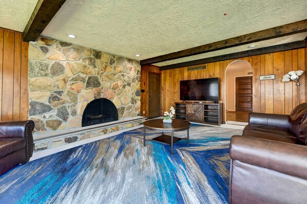 A living room with a stone fireplace, leather sofas, a flat-screen TV, and a blue and white patterned carpet.
