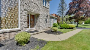 A stone house with a front door, a small front yard with a pathway, and a tree with red leaves. - Spacious Buffalo Brick Home w/ Backyard! (Buffalo)