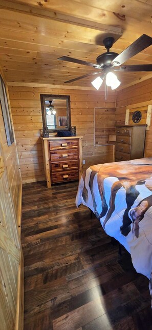 A wooden cabin bedroom with a bed, dresser, and a ceiling fan.