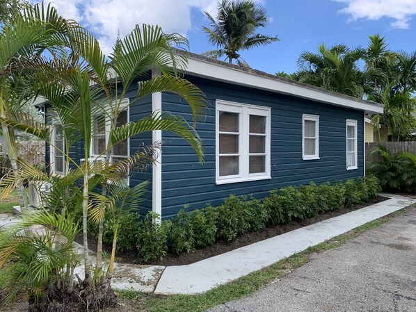 A single-story house with a dark blue exterior, white trim, and a front yard with palm trees and shrubs.