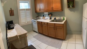 A compact kitchen with wooden cabinets, a sink, a stove, and a coffee maker. - Cheerful Cottage Close to the Beach! (Lake Worth)