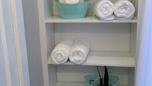 A bathroom with white shelves holding towels, a teal basin, and a bottle of hand soap. - Cheerful Cottage Close to the Beach! (Lake Worth)