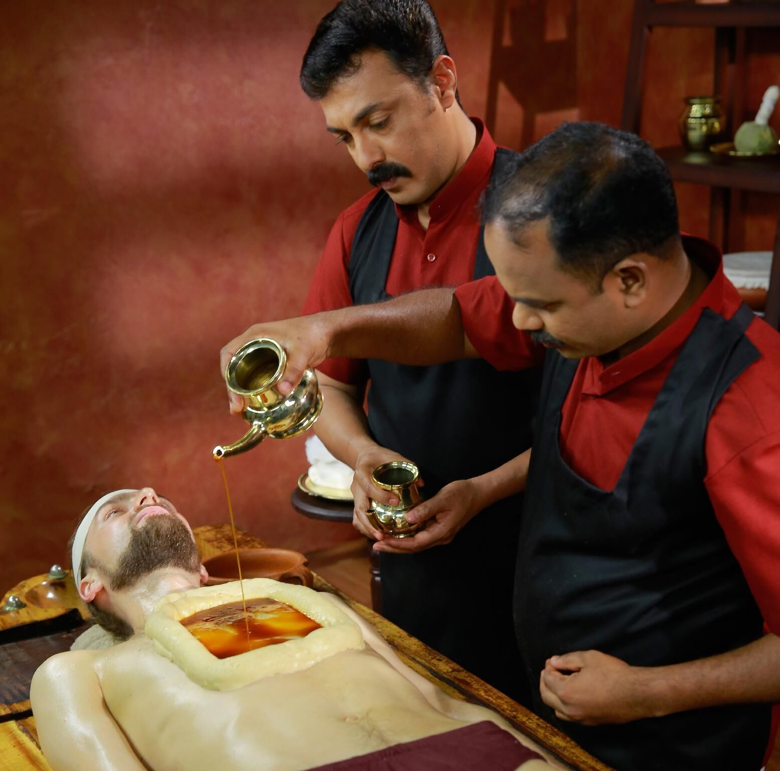 A person lying on a treatment table receiving a liquid from two individuals.