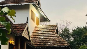 A traditional two-story building with a tiled roof, wooden balconies, and a well-maintained garden.