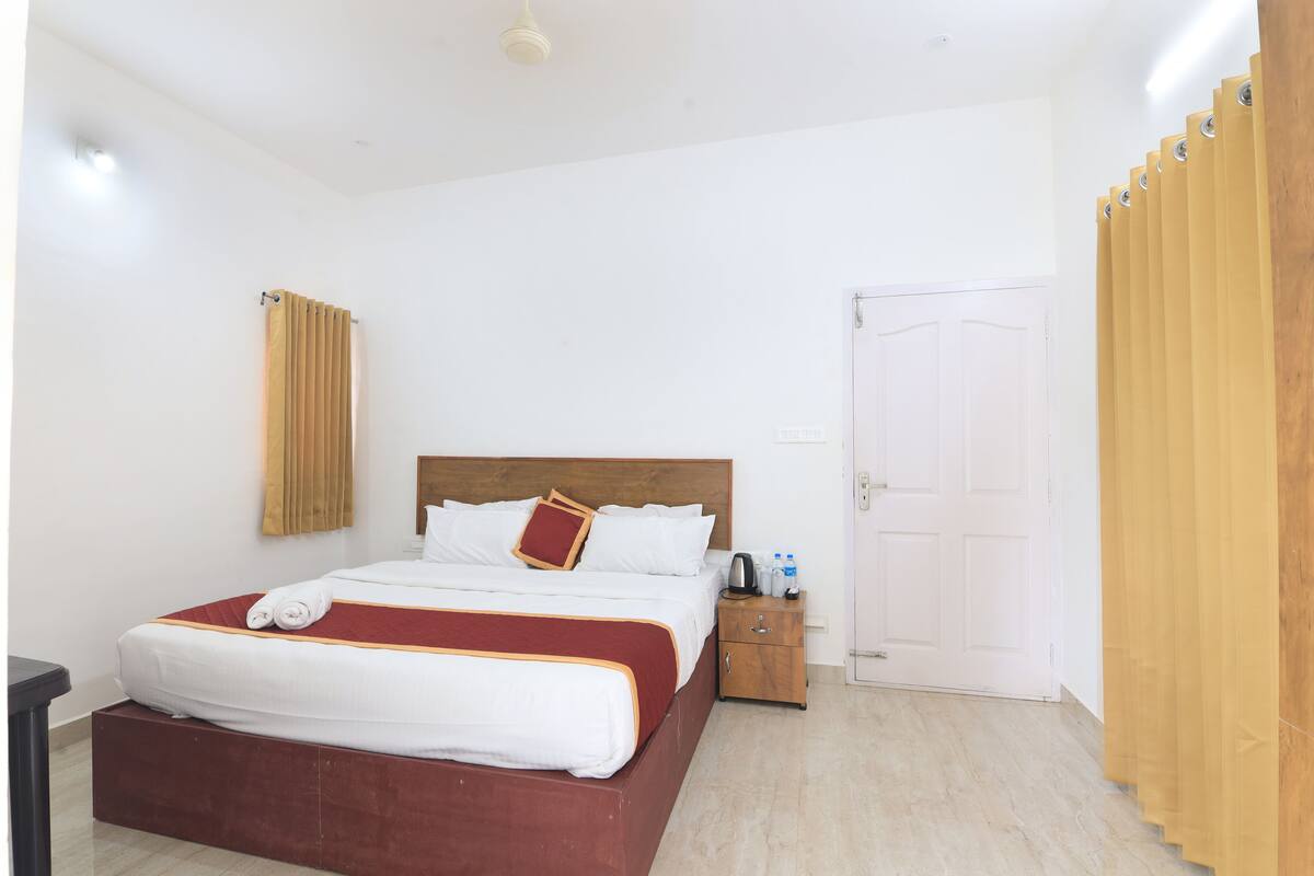 Una habitación de hotel con una cama grande, una mesita de noche de madera, una puerta blanca y una cortina de madera.