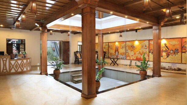 A spacious lobby with a high ceiling, wooden columns, a reception desk, and a large mural on the wall.