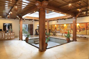 Un vestíbulo espacioso con techo alto, columnas de madera, una recepción y un gran mural en la pared.