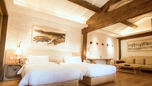 Ein Hotelzimmer mit zwei Betten, Holzboden, Steinwand und einem Gemälde über den Betten.