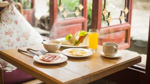 Ein Frühstücksbrett mit Eiern, Speck, Toast, Saft und Kaffee auf einem Holztisch neben einem Fenster.