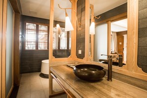 Een moderne badkamer met een houten wastafelmeubel, een grote spiegel en een zwarte kom op het aanrecht.