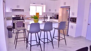 Una cucina moderna con mobili bianchi, un'isola centrale con sgabelli da bar, un piano cottura in acciaio inossidabile e un frigorifero.