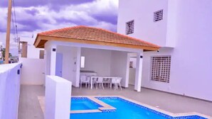 Un edificio bianco con tetto in tegole, una piscina e un patio con tavolo e sedie.