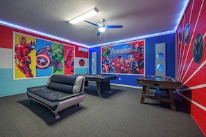 A room with a pool table, a sofa, and Avengers-themed wall art.