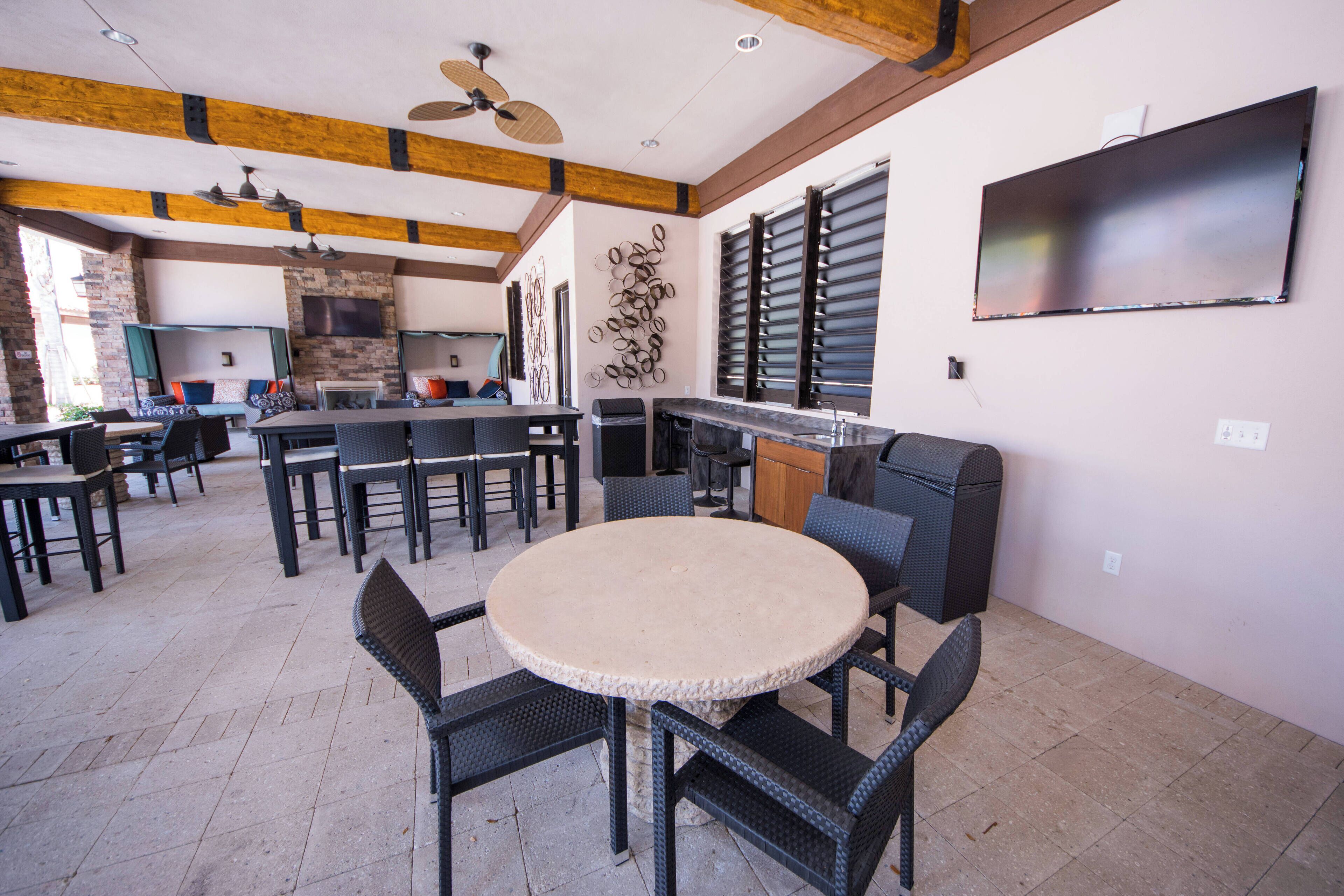 An outdoor dining area with round tables and chairs, a ceiling fan, and a TV mounted on the wall.