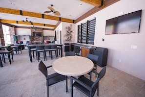 An outdoor dining area with round tables and chairs, a ceiling fan, and a TV mounted on the wall.