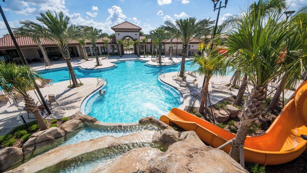 Une grande piscine extérieure avec un toboggan, entourée de palmiers et de chaises longues.