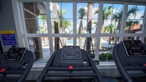 Trois tapis de course sont installés dans une pièce dotée de grandes fenêtres donnant sur des palmiers et une piscine.