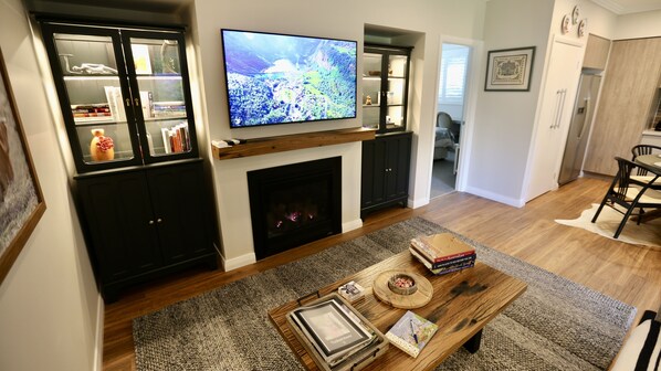 A living room with a fireplace, a television mounted above it, and a dining area with a table and chairs. - Self Contained Cottage in Bowral with Fireplace (Bowral)
