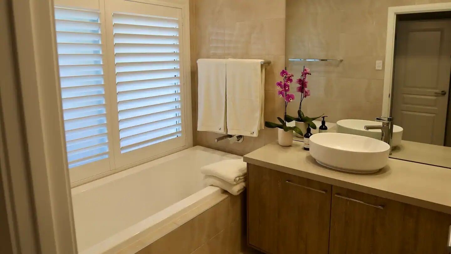 A bathroom with a bathtub, a sink with a large mirror, and a window with blinds.